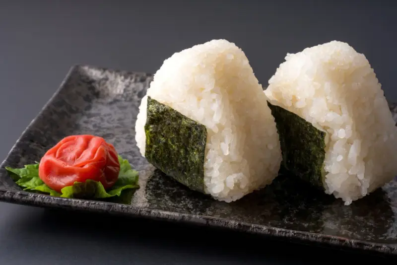 Deux onigiri algue sur une assiette avec une prune salée.