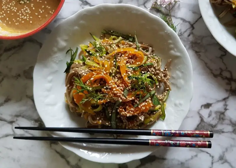 Salade de nouilles soba colorée avec des carottes, des courgettes et des graines de sésame, servie avec une sauce crémeuse.